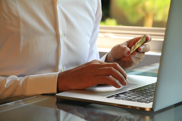Muž v bílé košili u notebooku drží platební kartu a nakupuje online na úspěšném e-shopu.